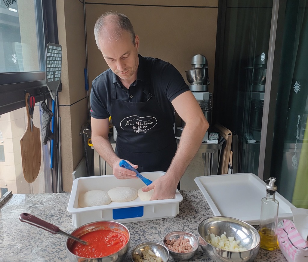 Primo piano di mani che schiacciano un panetto di impasto lievitato su una superficie infarinata per creare la base della pizza.