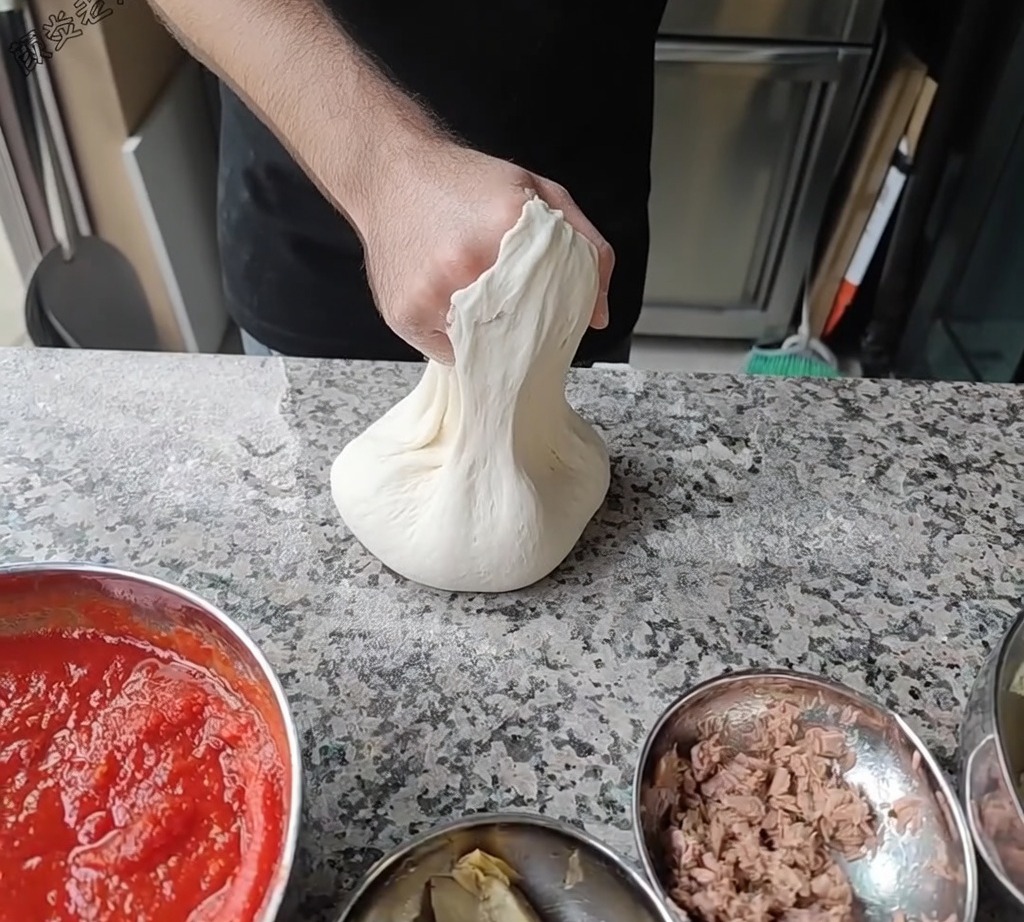 Lo chef che stende la pizza facendola ruotare sulle nocche per raggiungere il diametro desiderato.