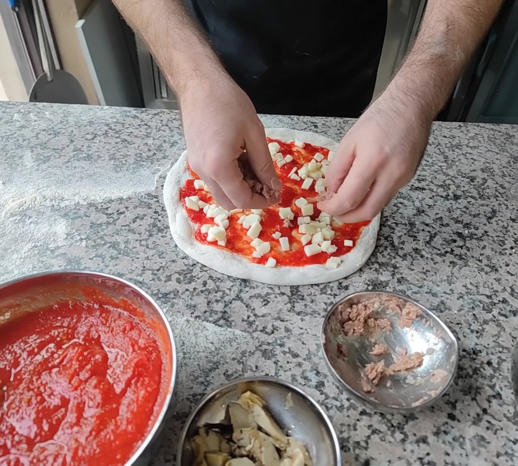 Aggiunta di scaglie di tonno e spicchi di carciofo sulla pizza come tocco finale.