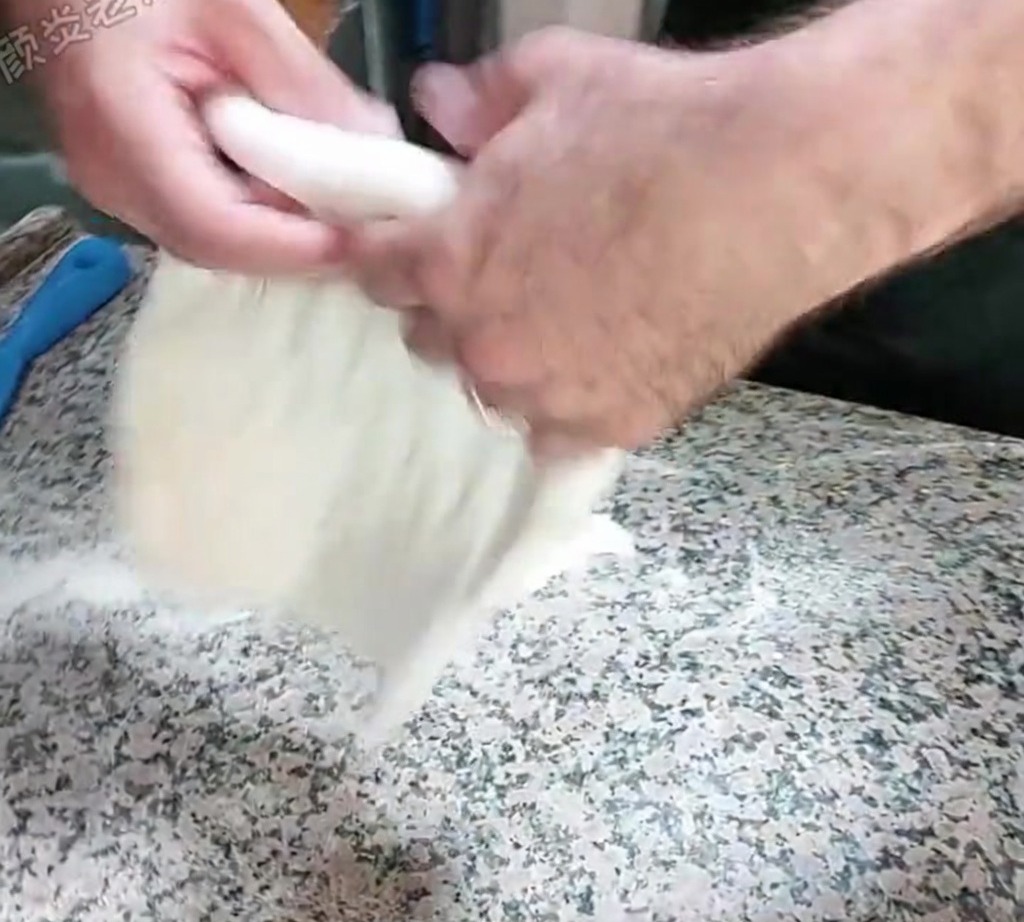 Impasto steso a mano con una tecnica di schiaffo su un piano di lavoro infarinato.