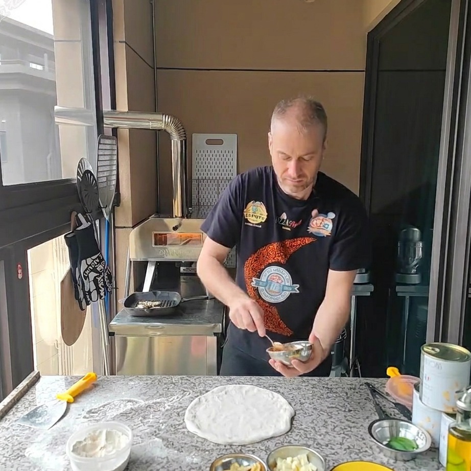 Un cucchiaio che spalma la salsa di pomodoro sulla base circolare della pizza.