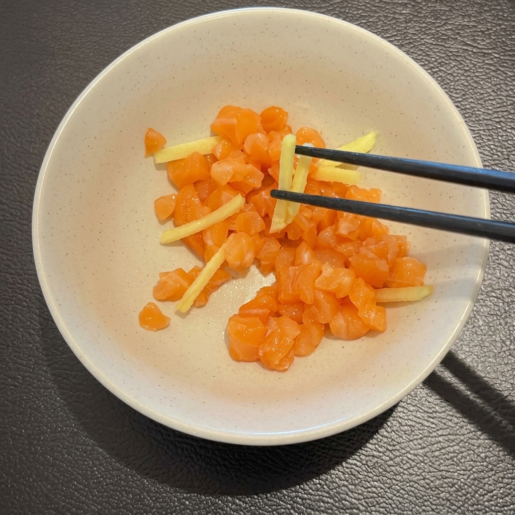 Salmone crudo a cubetti e zenzero a julienne mescolati con le bacchette in una ciotola bianca.