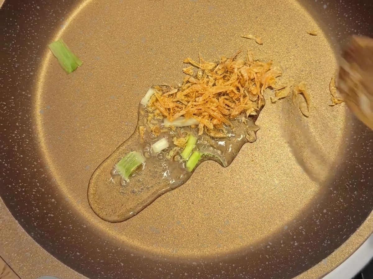 Gamberetti secchi e cipollotto a fette saltati delicatamente in olio in una padella bassa.