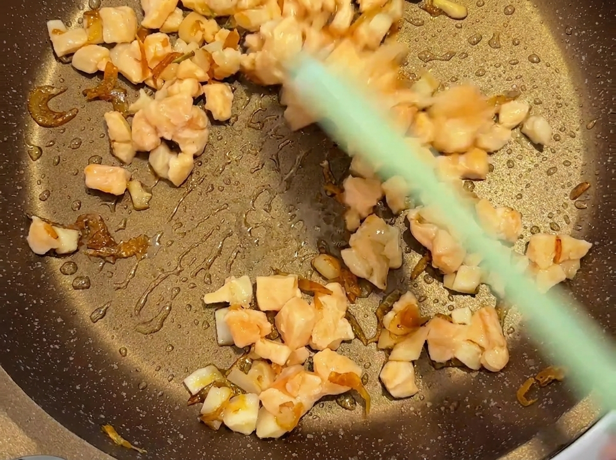 Una spatola verde che mescola salmone a cubetti e gamberetti secchi in una padella calda.