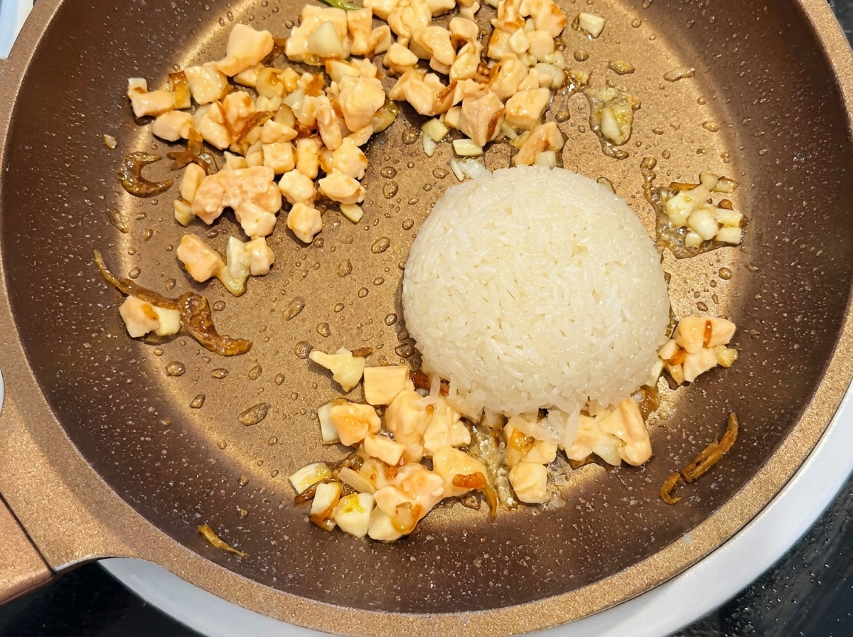 Un misurino di riso bianco crudo lavato e salmone crudo a cubetti posti in una padella accanto al composto di gamberetti saltati.