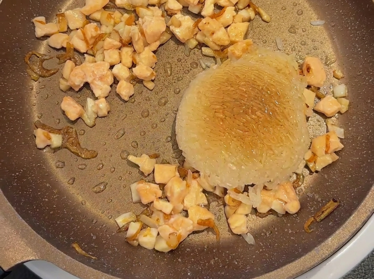 Salsa di soia per bambini spruzzata su un misurino di riso bianco e salmone a cubetti in una padella.