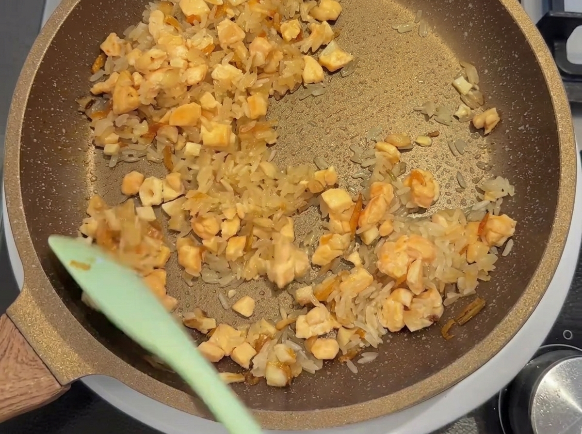 Riso bianco, salmone a cubetti e altri ingredienti saltati insieme in una padella.