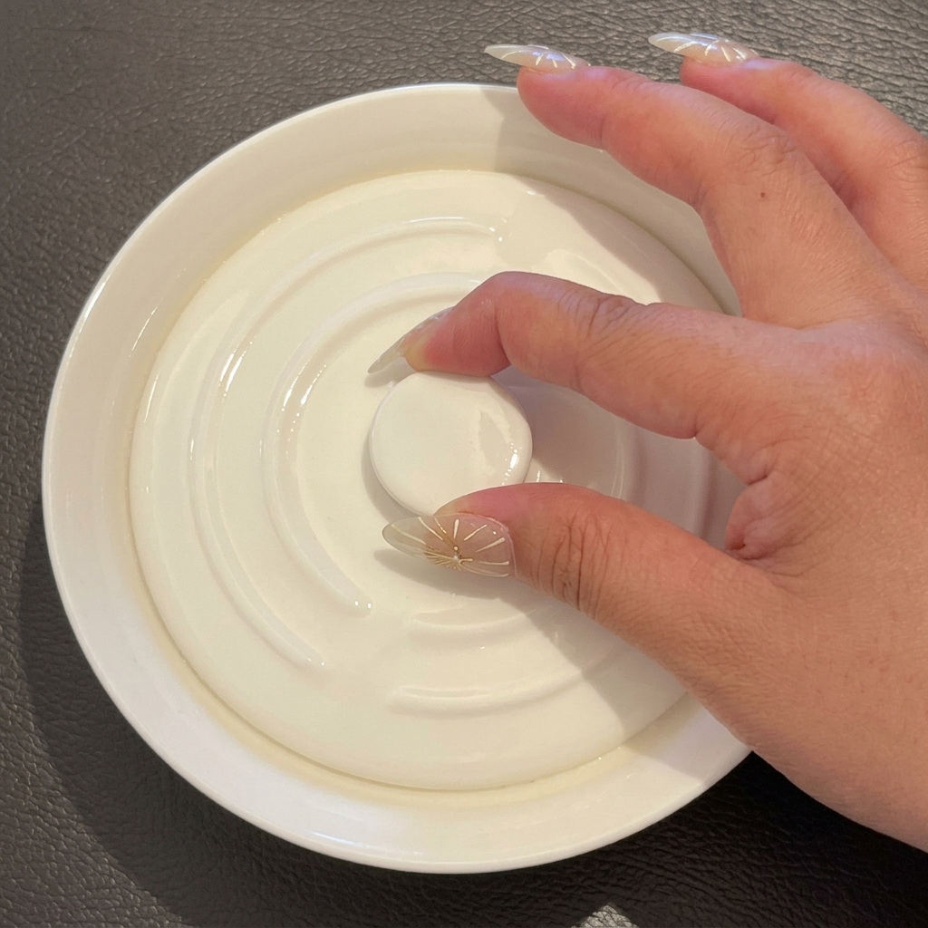Una mano che posiziona un coperchio di ceramica bianca sulla ciotola contenente il riso e lacqua.
