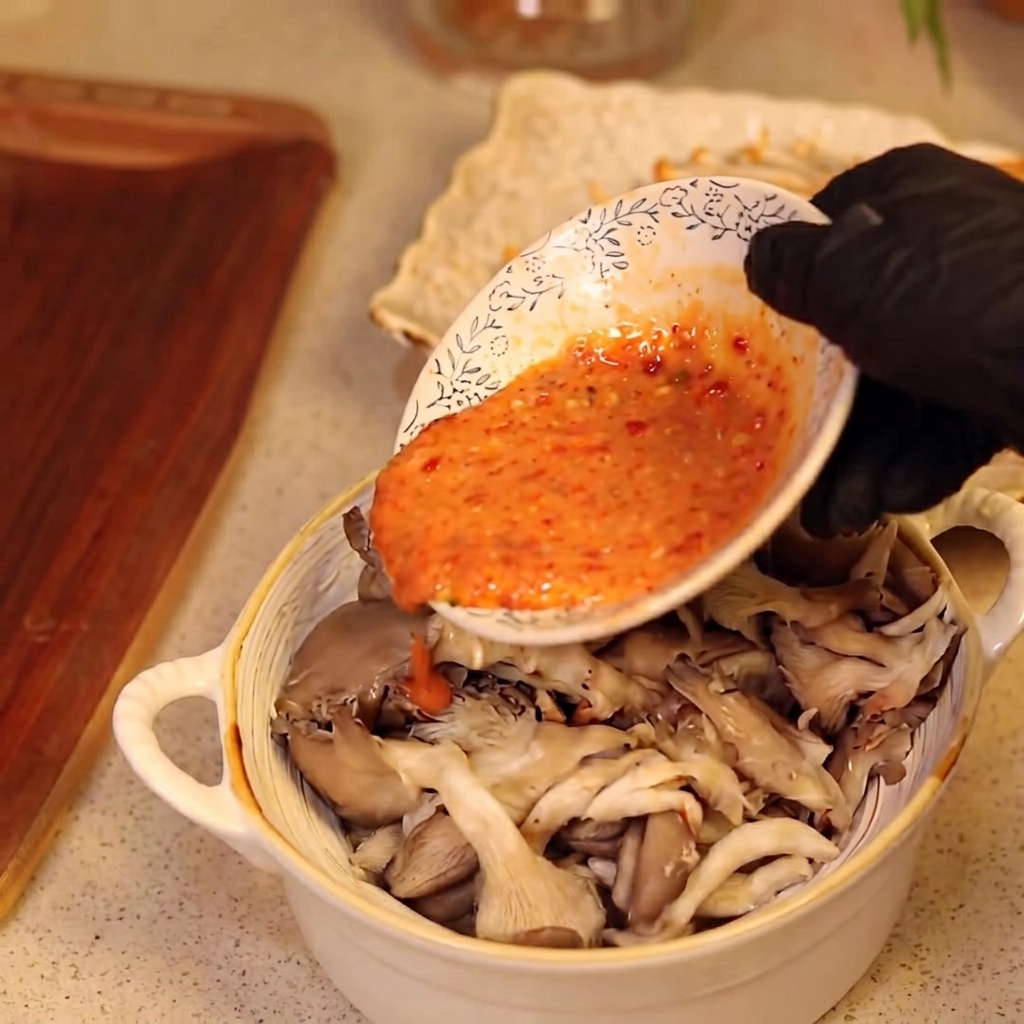 Mano guantata che versa la pastella sui funghi.