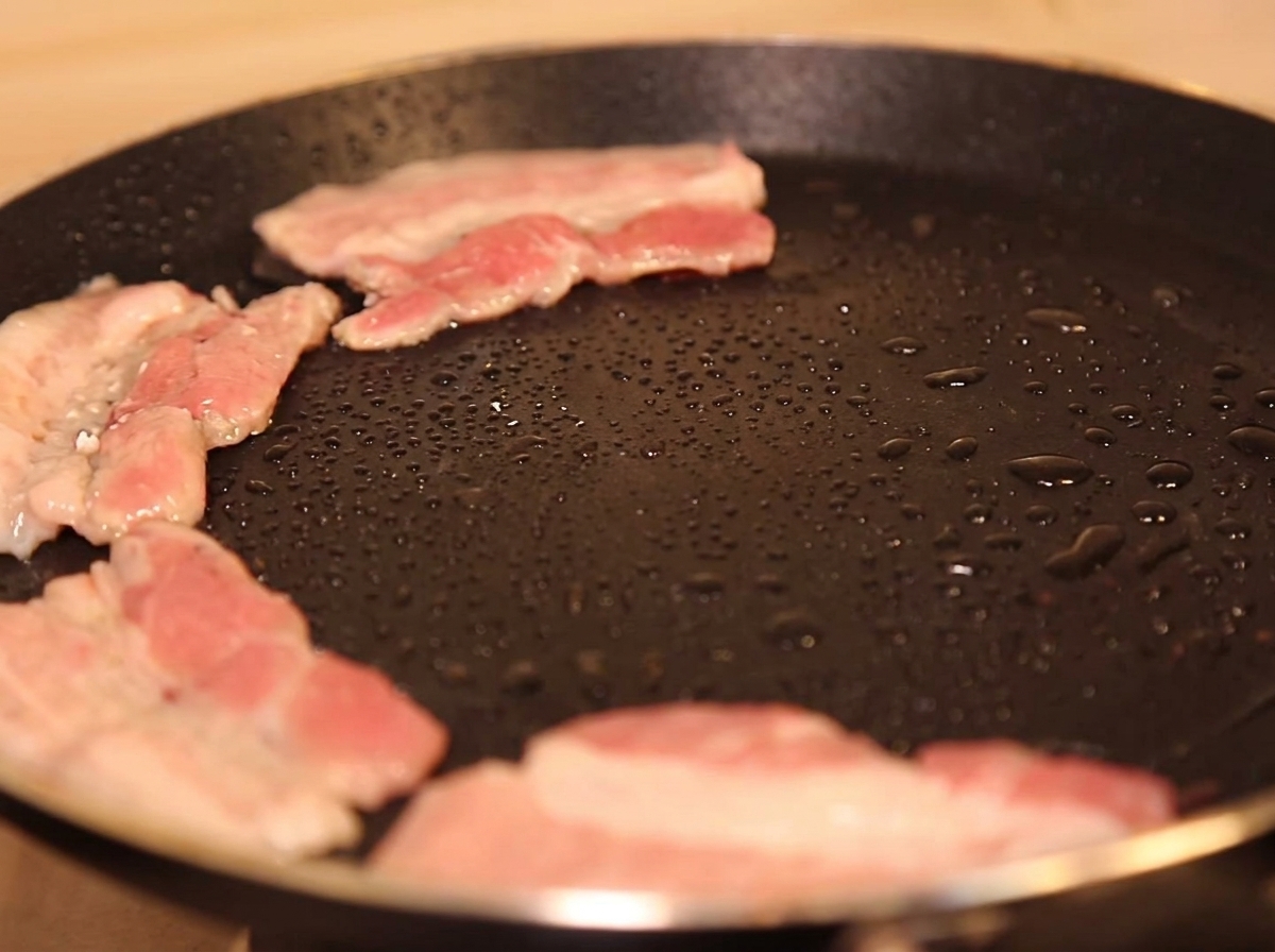 Fette di pancetta che sfrigolano in padella.