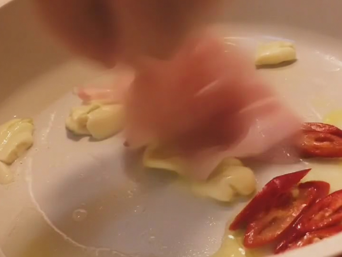 Strisce di pancetta che saltano in una padella chiara con aglio e fette di peperoncino rosso.