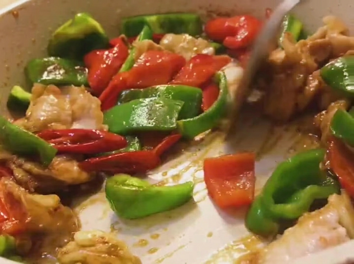 Un mix di pancetta, peperoni verdi e peperoni rossi saltati in padella con una spatola di legno.