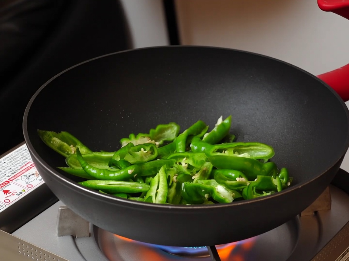 Peperoni a fette saltati in una padella antiaderente su un fornello a gas portatile.