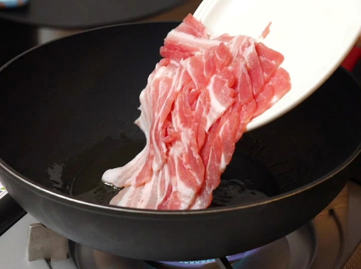 Pancetta cruda a fette sottili aggiunta da un piatto bianco in una padella calda oleata.