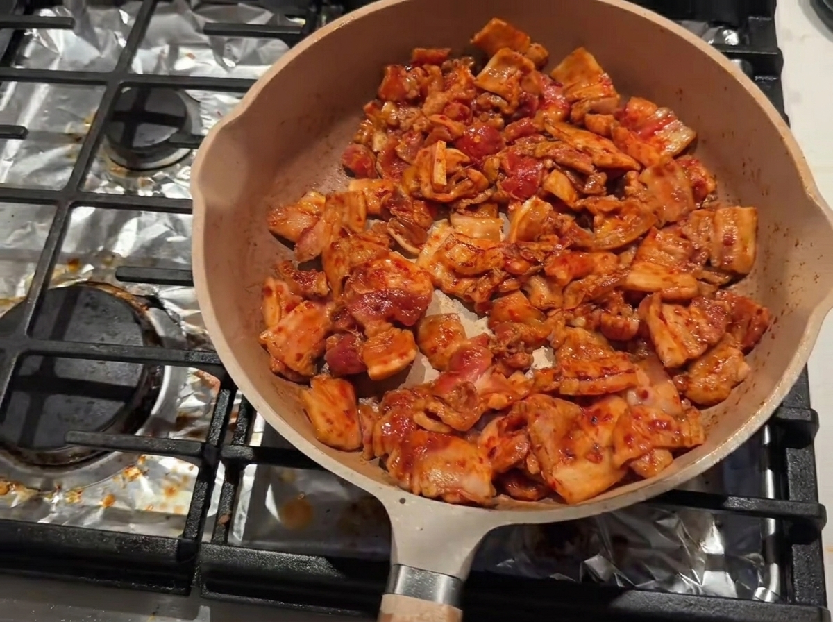 Pancetta che rosola in una padella con vino da cucina aggiunto lungo il bordo interno.