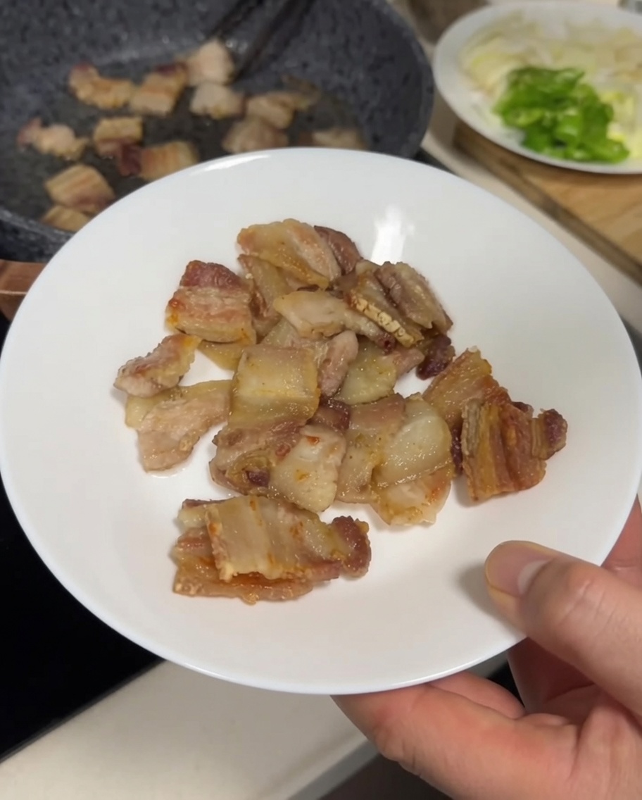 Pezzi di pancetta croccante dorata trasferiti dalla padella a un piatto bianco con pinze di metallo.
