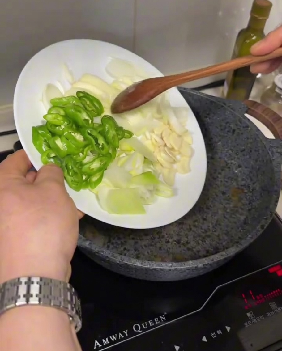 Peperoncini verdi affettati, cipolle bianche e aglio aggiunti da un piatto in una padella calda con olio.