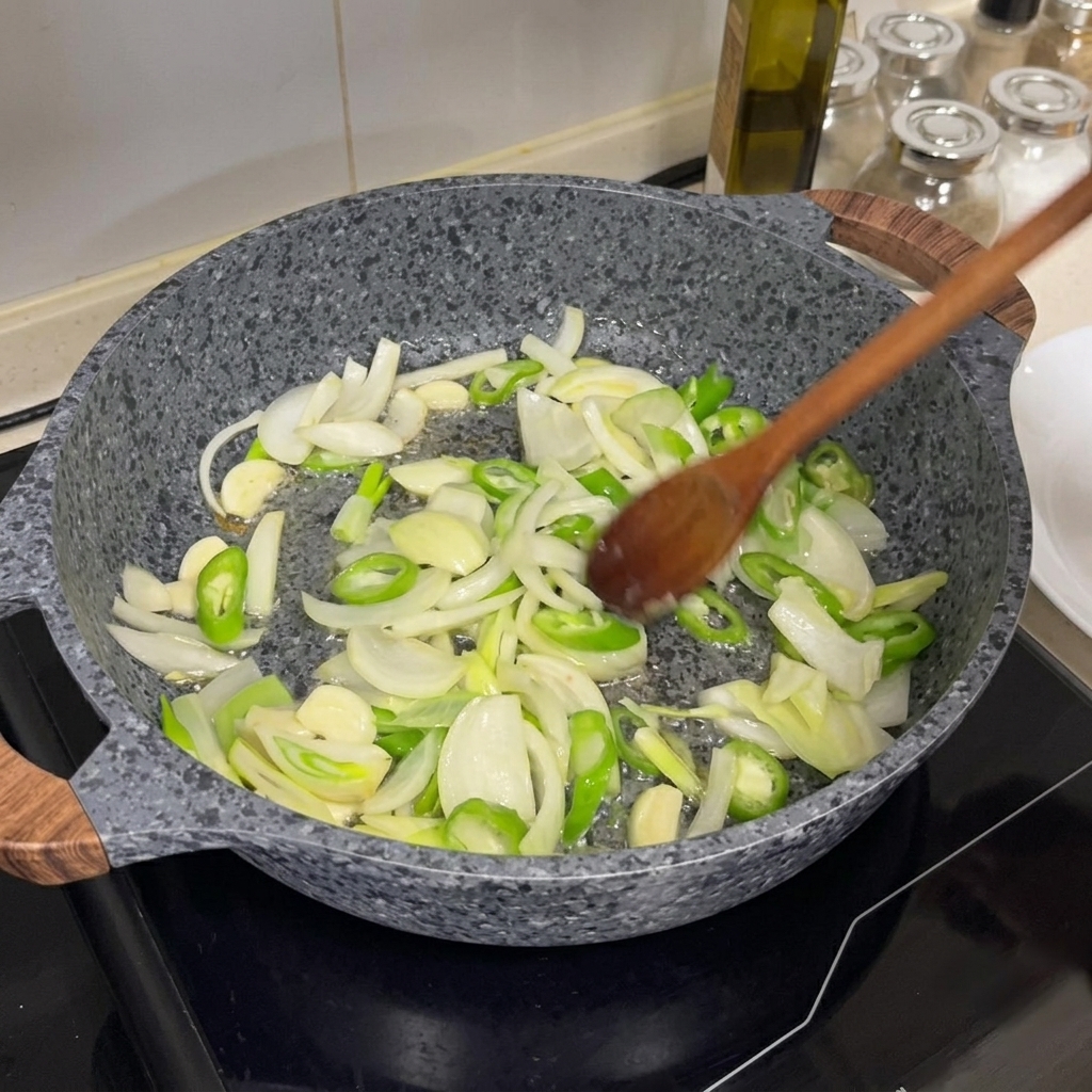 Cipolle, peperoncini verdi e aglio saltati in una padella calda con un cucchiaio di legno.