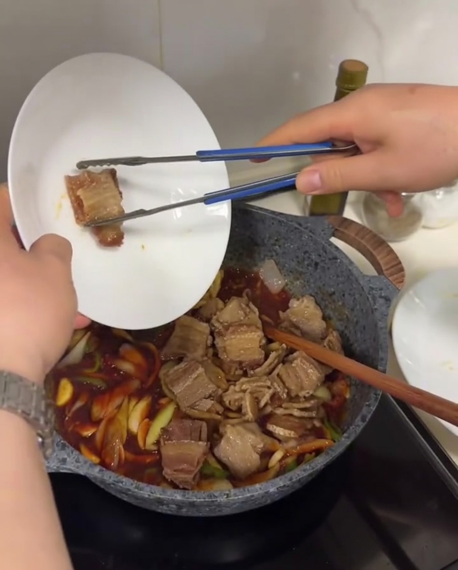 Fette di pancetta croccante aggiunte in una padella con cipolle, peperoni e una ricca salsa rossa gorgogliante.