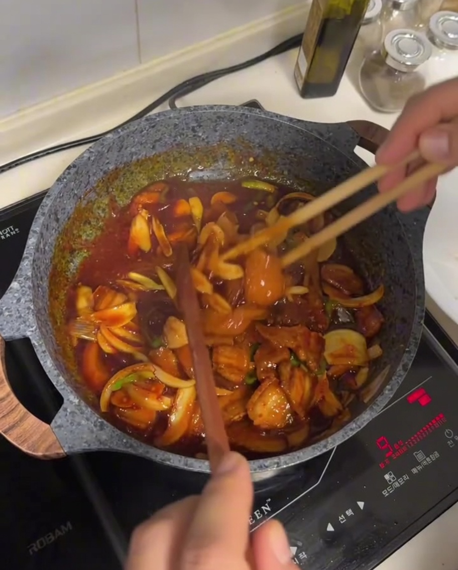 Mix di pancetta e verdure saltato in una salsa rossa scura e lucida usando bacchette di legno in una padella antiaderente.