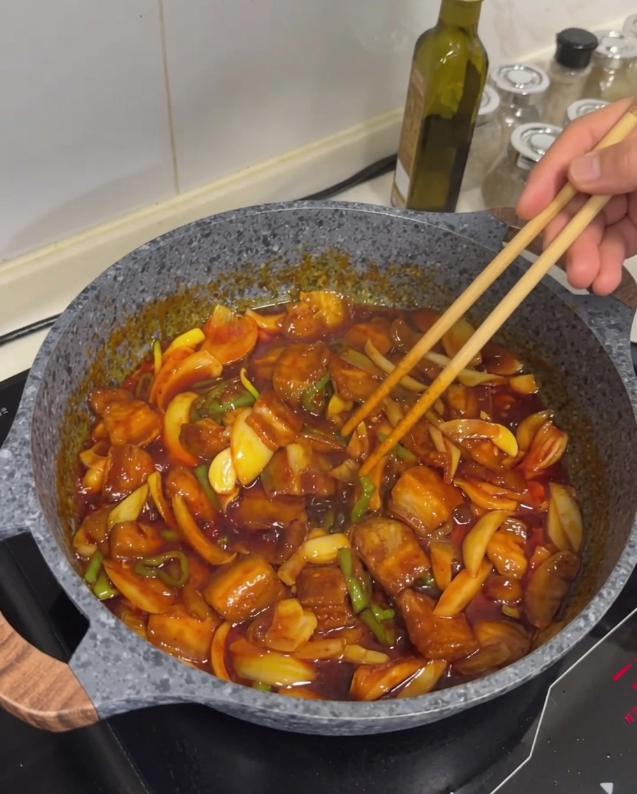 Il piatto finale di maiale saltato piccante con carne dorata, salsa lucida e una spolverata di semi di sesamo bianco sopra.