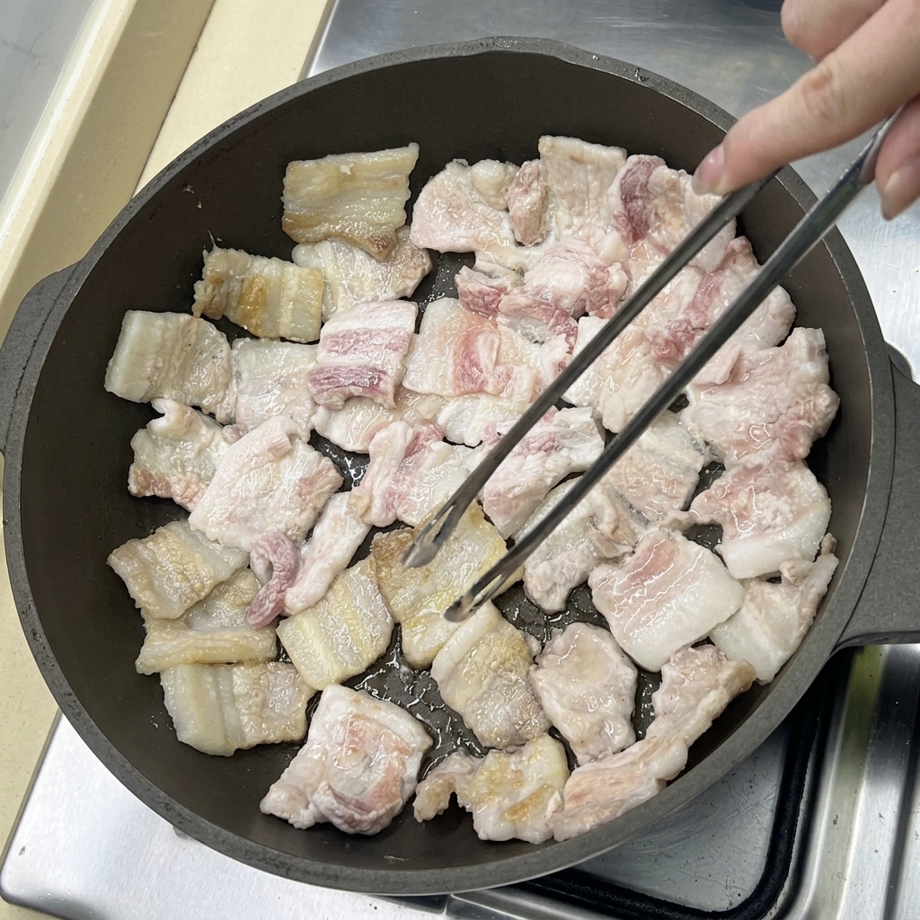 Fette di pancetta che friggono in padella, diventando dorate mentre il grasso si scioglie.