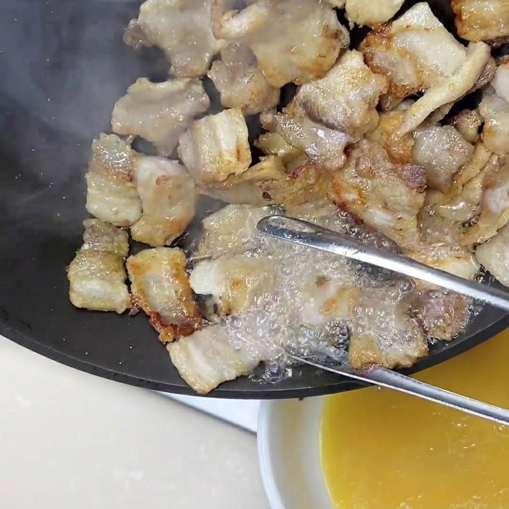 Pinze che tengono le fette di pancetta mentre il grasso dorato in eccesso viene versato fuori dalla padella.