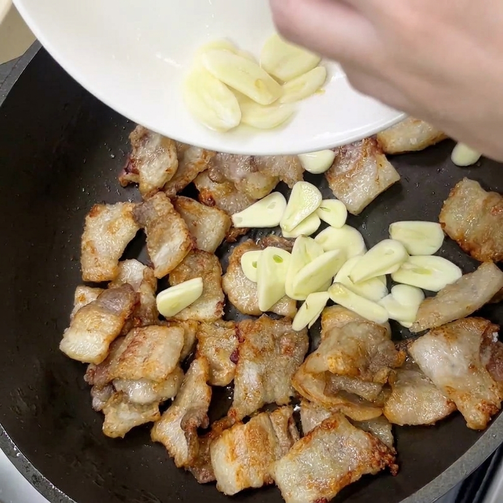 Fette di aglio fresco aggiunte in padella con la pancetta dorata.