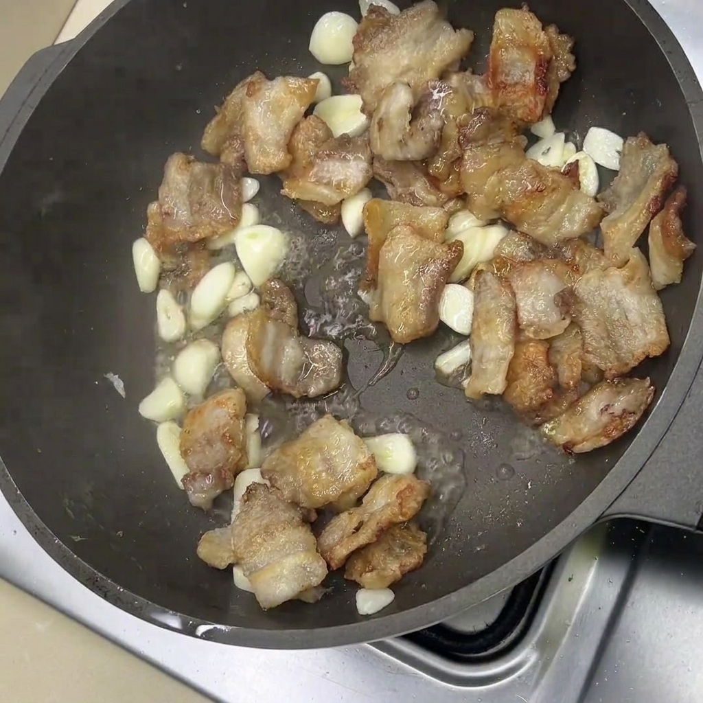 Fette di pancetta fritta e spicchi daglio che sfrigolano in padella.
