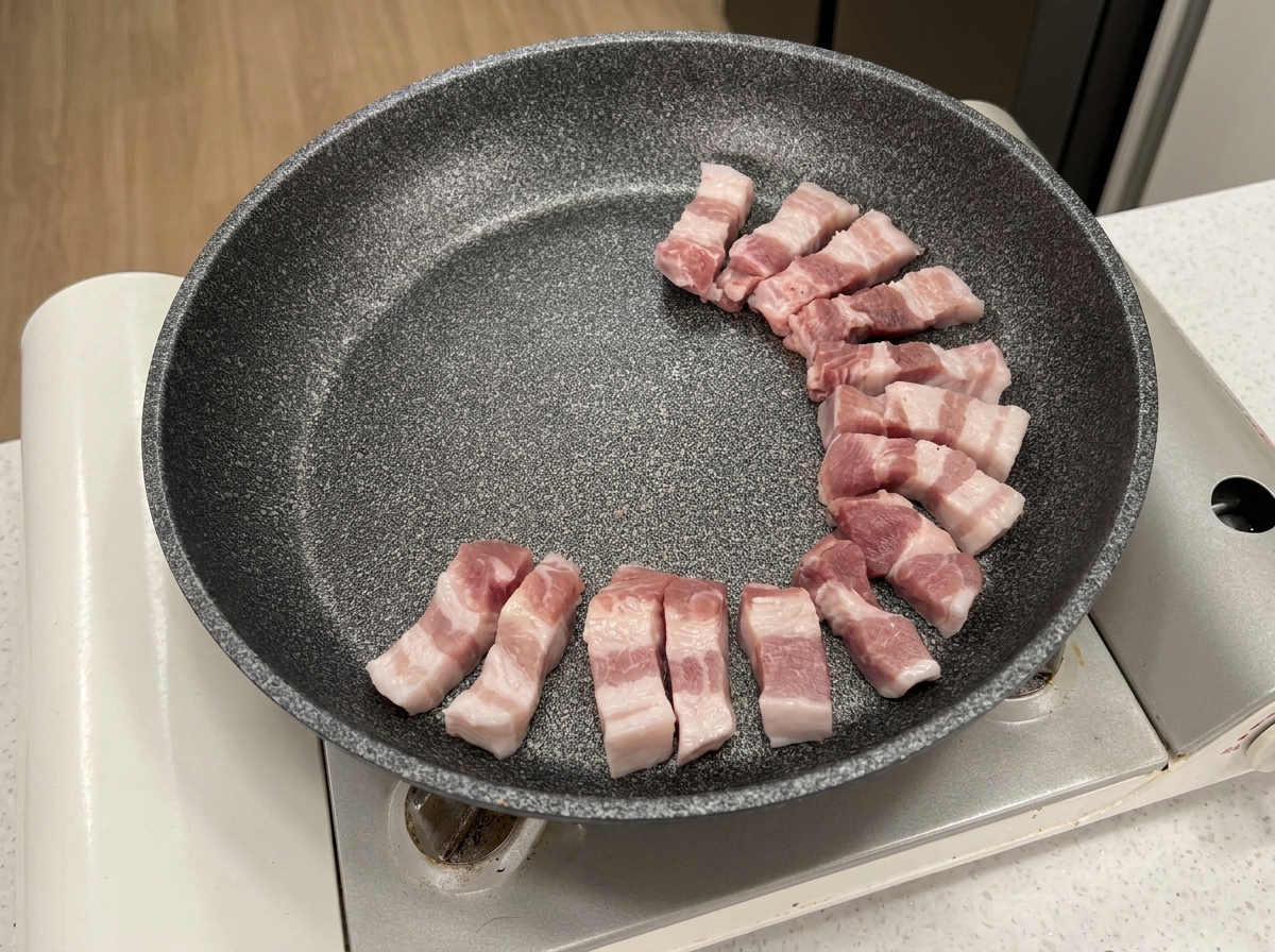 Fette di pancetta cruda disposte in cerchio in una padella antiaderente grigia.