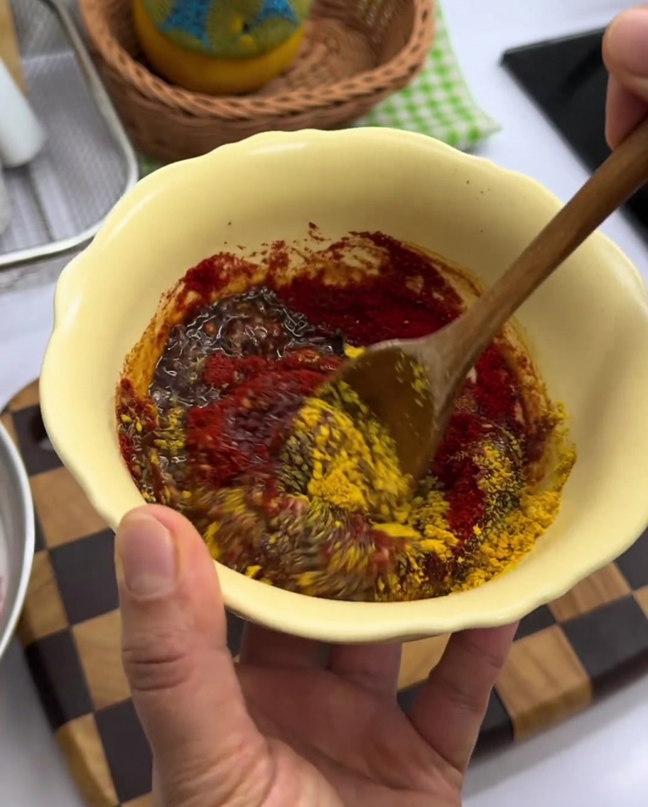 Pasta di spezie rossa densa mescolata in una ciotola gialla.