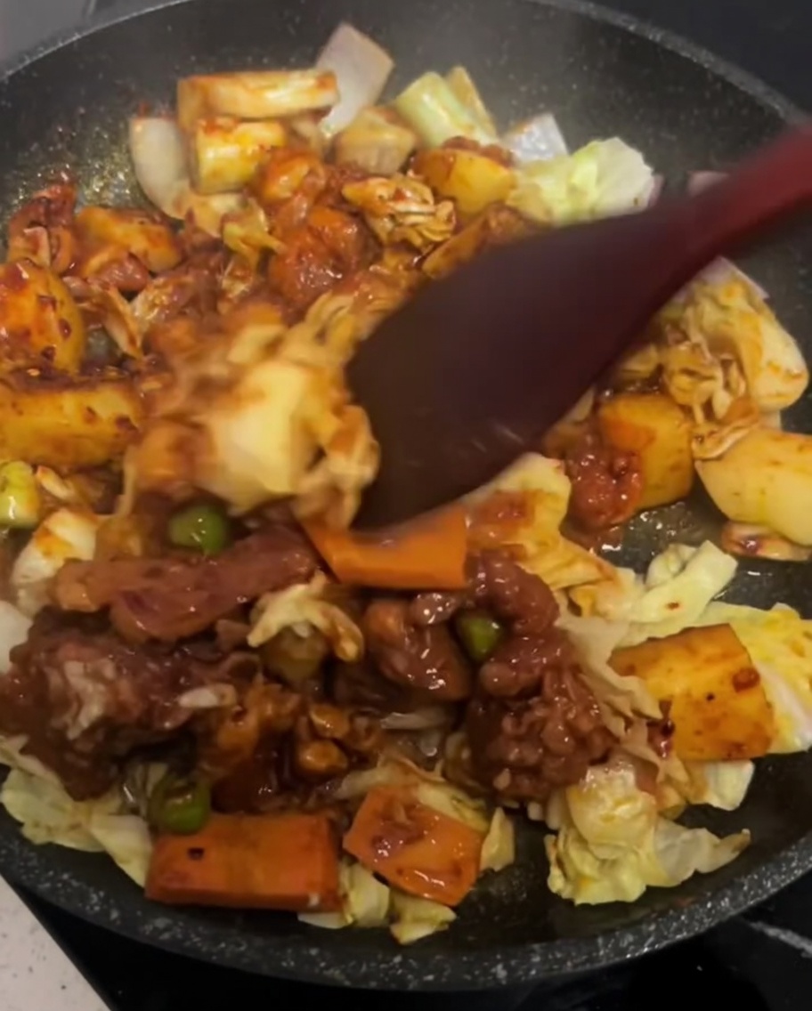 Una spatola mescola delicatamente il pollo e le verdure in una padella calda.