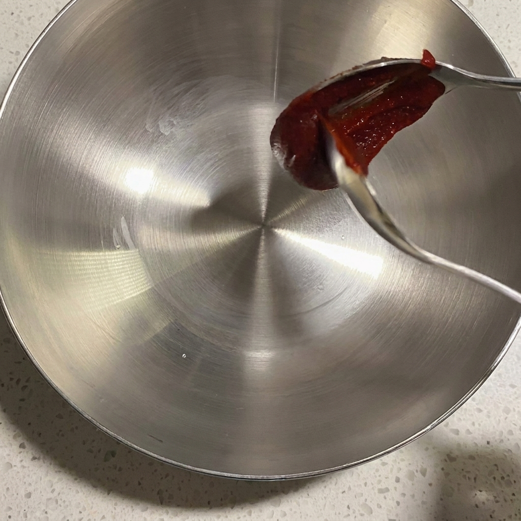 Un primo piano di una ciotola di metallo con vari condimenti e salse pronti per essere mescolati.