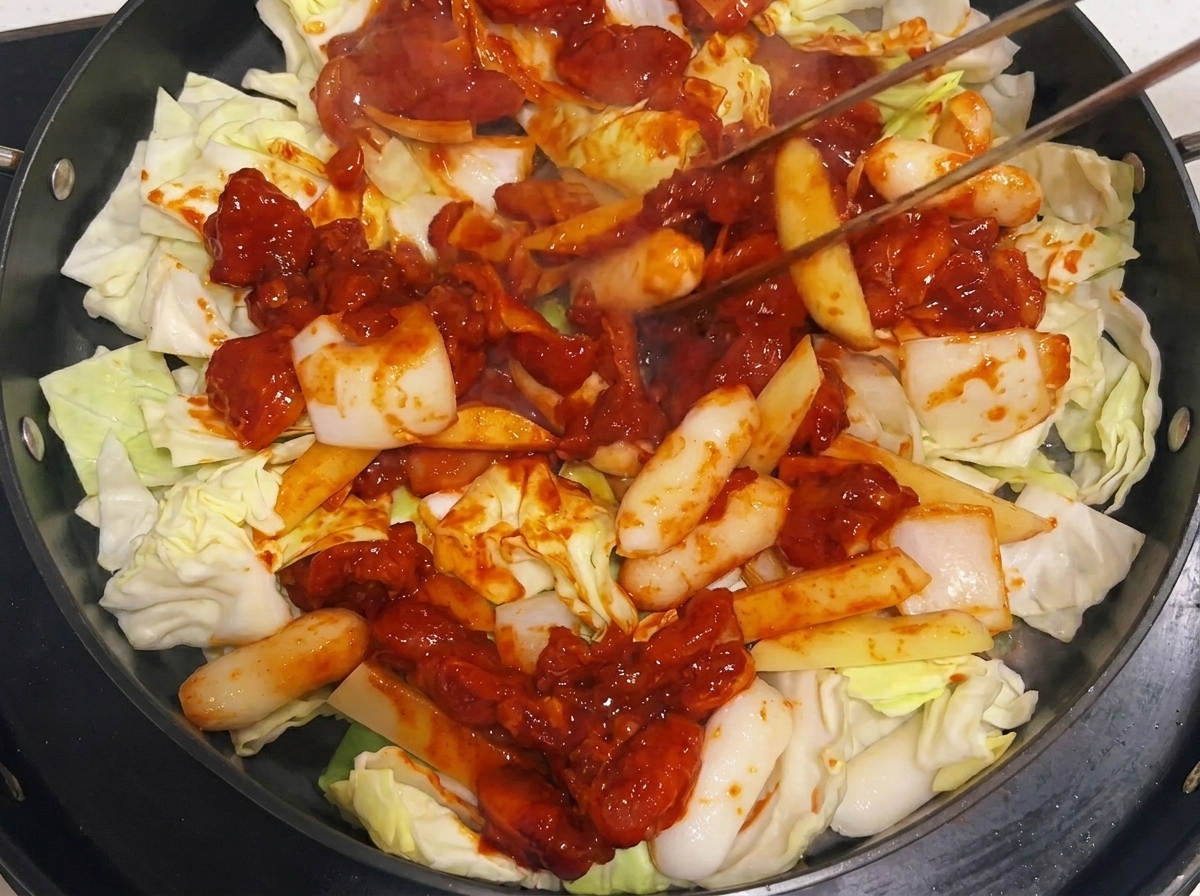 Pinze che mescolano il composto di pollo e verdure nella padella durante la cottura.