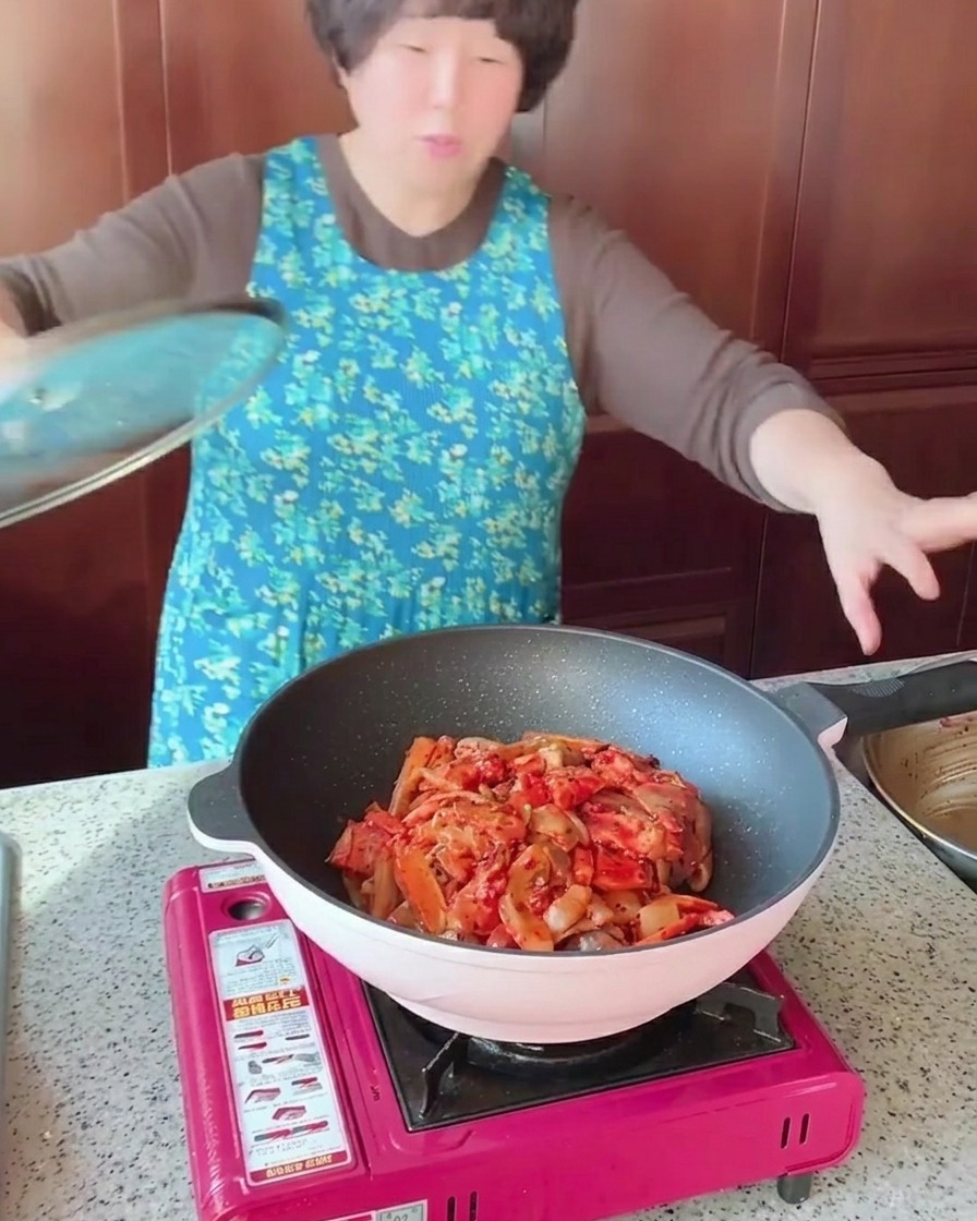 Una padella piena di pancetta di maiale saltata, calamari e verdure coperta da un coperchio di vetro trasparente.