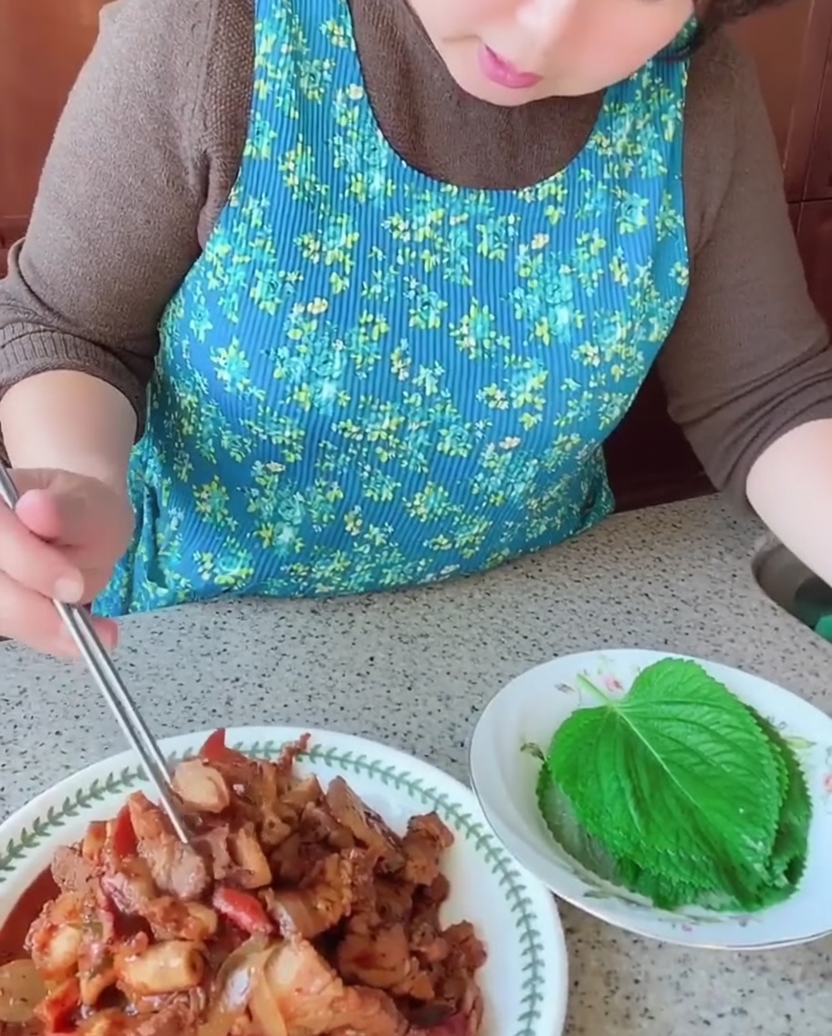 Una persona che utilizza le bacchette per posizionare un pezzo di pancetta e un calamaro cotti su una foglia fresca di perilla verde.