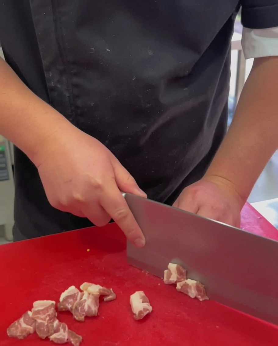 Fette di pancetta cruda disposte su un tagliere rosso.