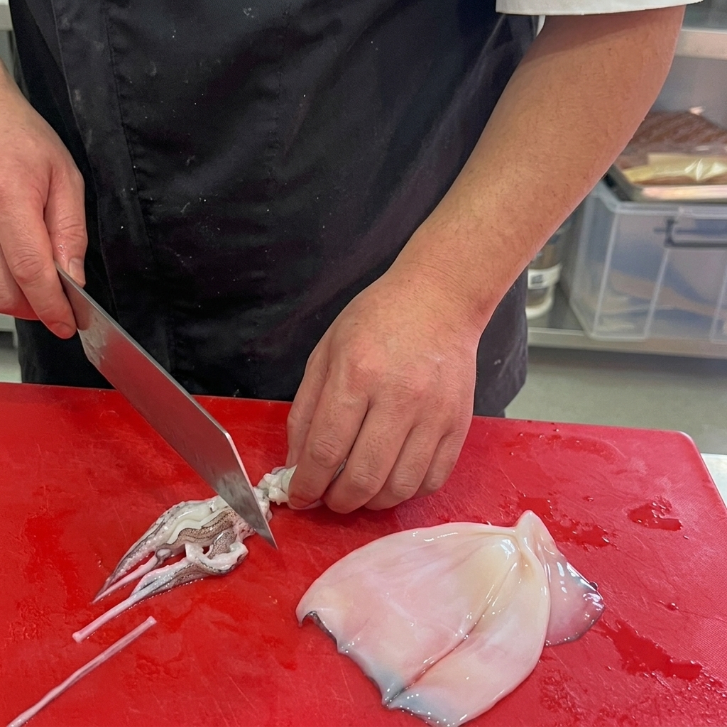 Calamari puliti tagliati ad anelli su un tagliere rosso.