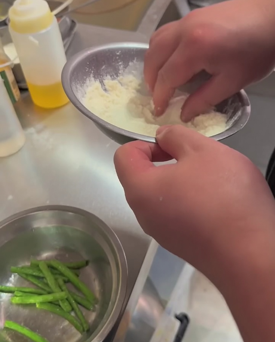 Fagiolini mescolati con farina e condimento in una ciotola di metallo.