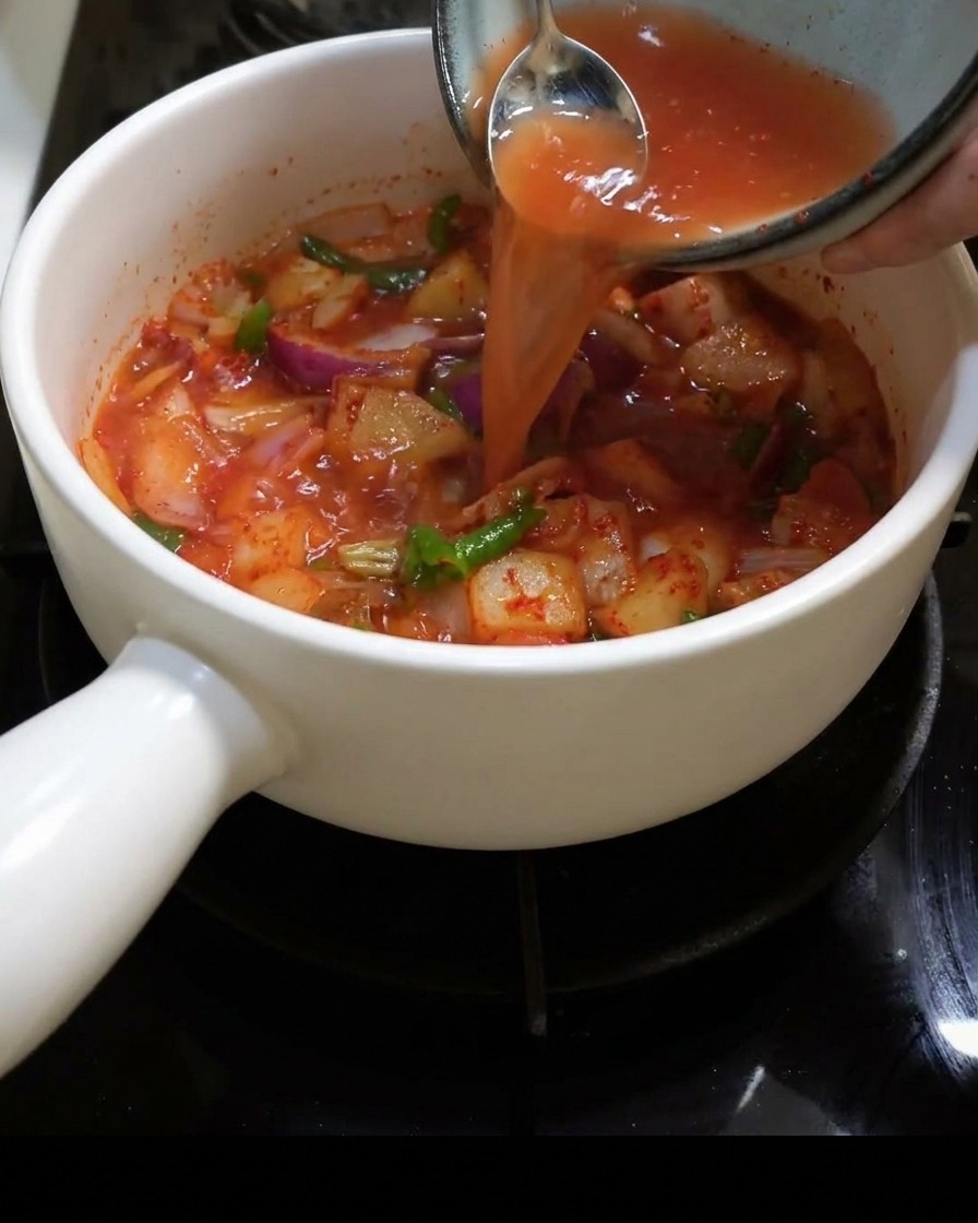 Lacqua viene versata nella pentola piena di kimchi e cipolle.