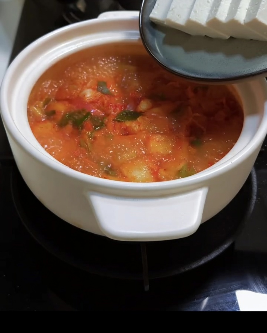 Fette di tofu vengono aggiunte alla zuppa rossa e bollente di kimchi.
