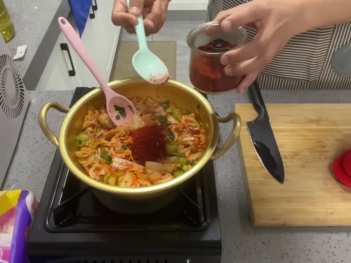 Un cucchiaio di vibrante peperoncino in polvere aggiunto al kimchi saltato.