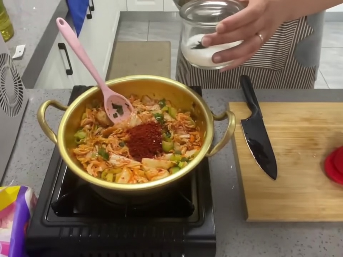 Un cucchiaio di zucchero bianco aggiunto al composto di kimchi condito nella pentola.