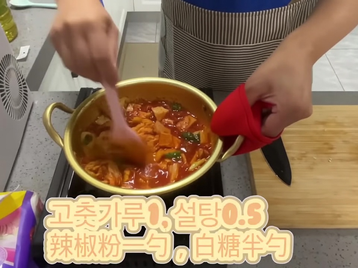Composto di kimchi condito mescolato insieme in una pentola con una spatola rosa.
