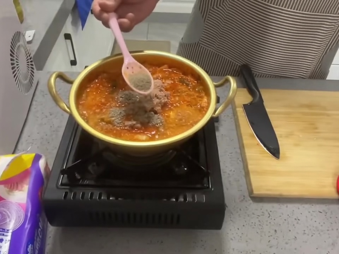 Dado di manzo in polvere cosparso da un cucchiaio in una pentola di stufato rosso di kimchi e tonno.