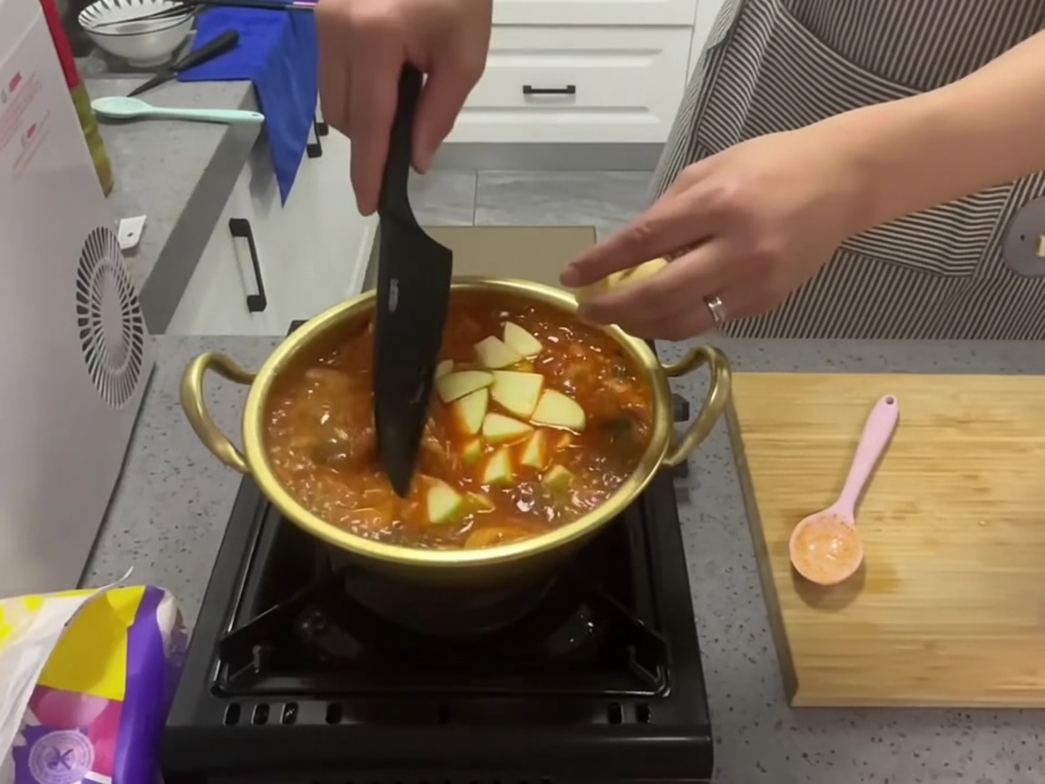 Fette di zucchina verde fresca aggiunte a una pentola di stufato di kimchi rosso bollente.