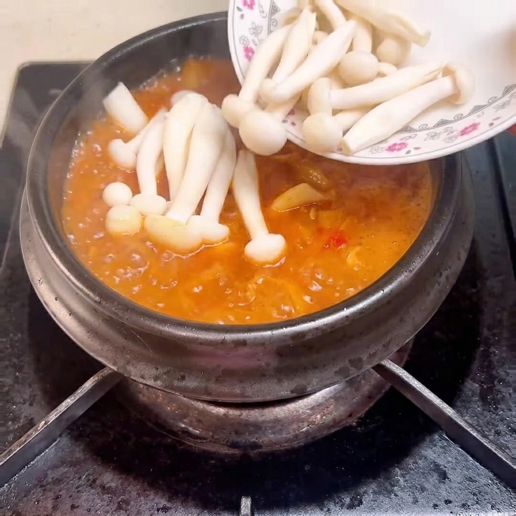 Funghi shimeji aggiunti alla zuppa in ebollizione nel tegame.
