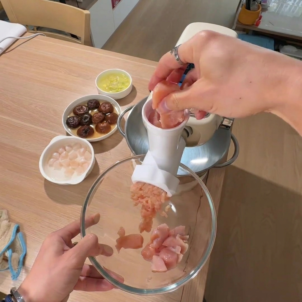 Una mano che posiziona pezzi di petto di pollo in una grande ciotola con le ciotole di funghi e capesante sullo sfondo.