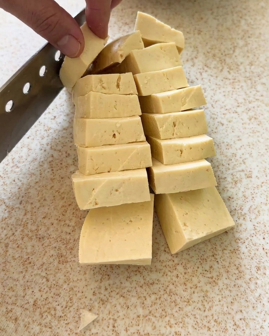 Un panetto di tofu tagliato in cubetti uniformi su un tagliere.