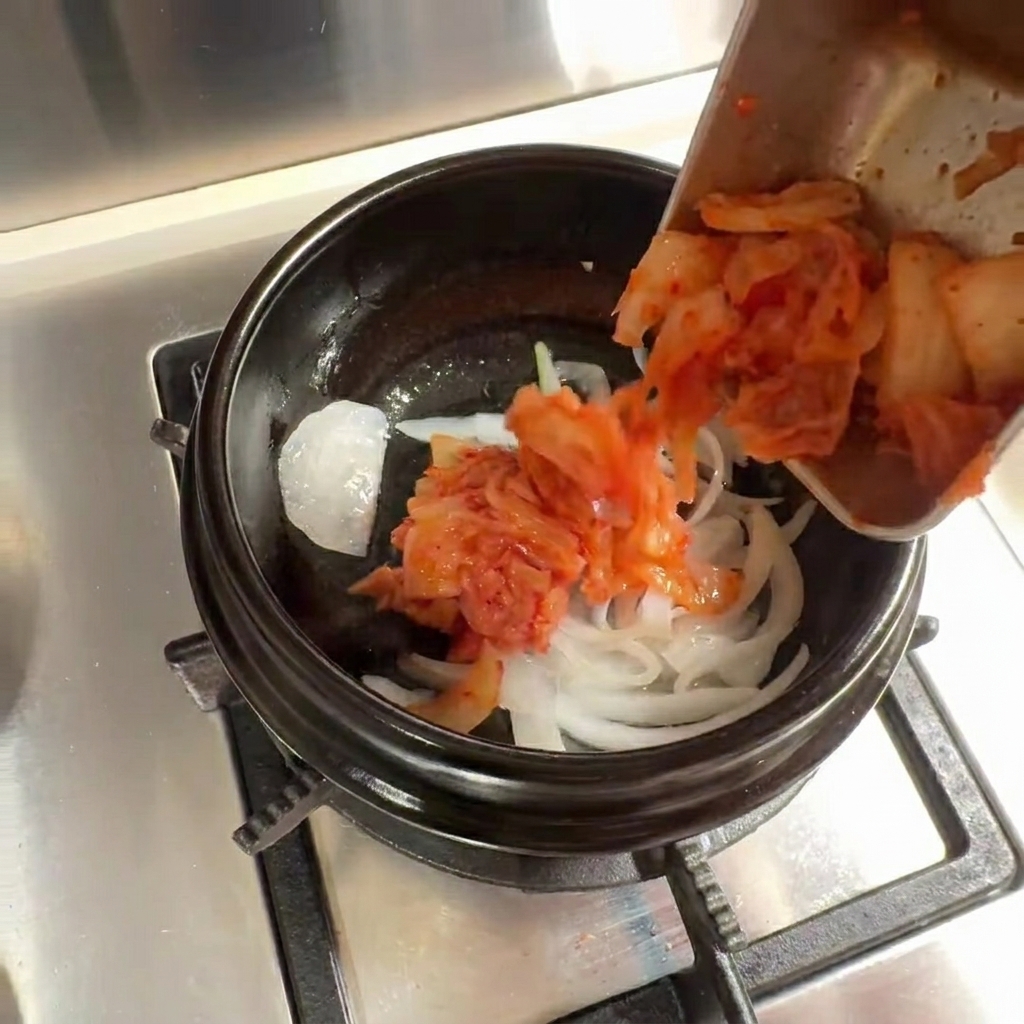 Kimchi aggiunto alle cipolle soffritte nella pentola di pietra.